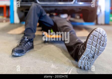 High angle of crop anonymous male mechanic lying on car creeper and examining details of automobile while working in modern service Stock Photo