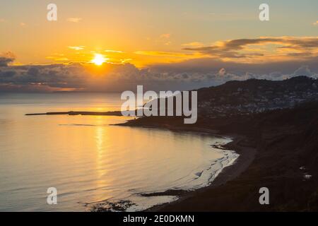 Charmouth, Dorset, UK.  31st December 2020.  UK Weather.  View from the cliff top at Charmouth of the moody sunset over seaside town of Lyme Regis on the Dorset Jurassic Coast on the last day of 2020.  Picture Credit: Graham Hunt/Alamy Live News Stock Photo