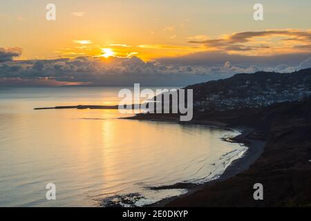 Charmouth, Dorset, UK.  31st December 2020.  UK Weather.  View from the cliff top at Charmouth of the moody sunset over seaside town of Lyme Regis on the Dorset Jurassic Coast on the last day of 2020.  Picture Credit: Graham Hunt/Alamy Live News Stock Photo