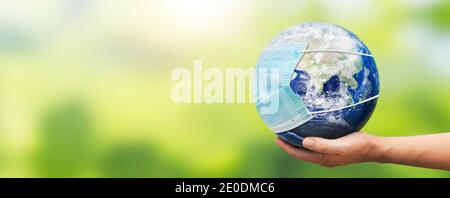 Hand holding Earth globe with face mask. World pandemic concept. Elements of this image furnished by NASA Stock Photo