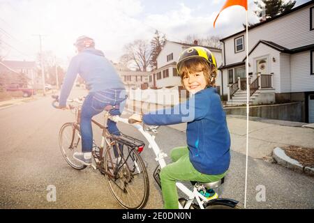 Portrait of a little boy ride on a tow tandem bike attached to father on urban street view from behind Stock Photo