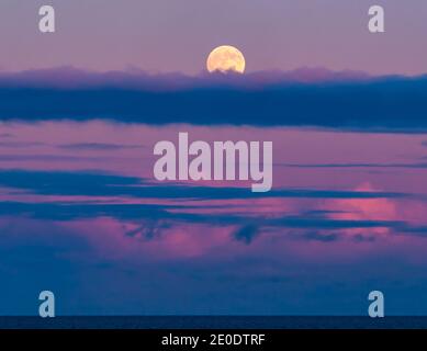 A full moon rises over the Firth of Forth with colourful pink clouds at sunset, Scotland, UK Stock Photo