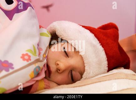 A little girl (6 yr old) asleep in bed with her christmas hat on