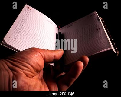 Notebook with a pen in a mans hand on a black background. Notebook for notes. Business weekly. Keep a diary. Business plan. Human hand. Writing pen. B Stock Photo