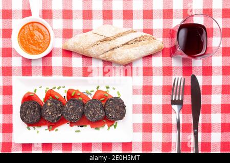 Slices of Spanish black pudding on piquillo peppers in white plate on a red checkered tablecloth . Spanish tapas. Stock Photo