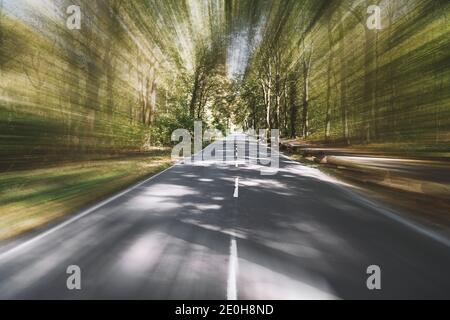 empty two-lane country road through woodland with motion blur speed effect - fast travel background with copy space Stock Photo