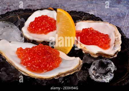 Fresh red salmon caviar  and slice of lemon in the  oyster shells on ice in vintage metal tray Stock Photo