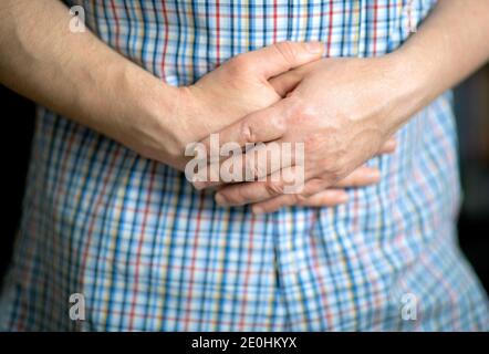 Man in a shirt holding hands on his stomach, closeup on the hands Stock Photo