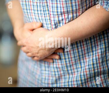 Man with stomach ache. Man in a shirt, holding hands on his stomach, closeup on the hands Stock Photo