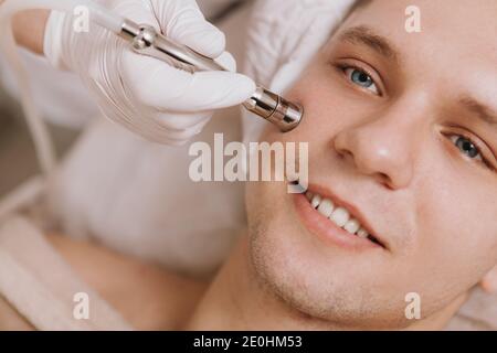 Cropped close up of a young cheerful man smiling while cosmetologist performing facial skincare treatment Stock Photo