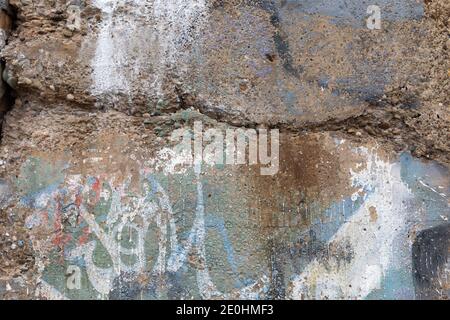 Crumbling concrete aggregate wall with traces of paint in blue, green, and white, horizontal aspect Stock Photo