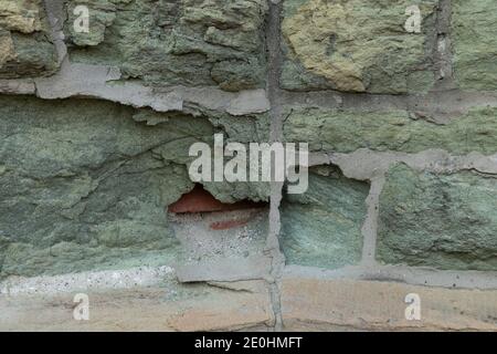 Green limestone wall eaten away to show brick beneath, effects of decay and pollution, horizontal aspect Stock Photo