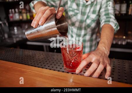 Close up of a male bartebder pouring a drink to the glass. Professional bartender preparing cocktail for a customer Stock Photo