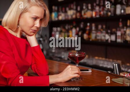 Cropped shot of a sad woman drinking at the bar. Depressed woman having a cocktail alone at the restaurant Stock Photo