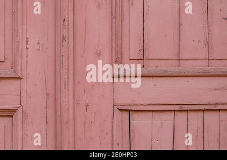 Fragment of an old wooden door painted with pink paint. A background from an old surface with cracked paint. Selective focus. Stock Photo