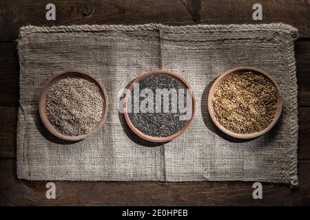 Sesame, chia and flax seeds in wooden dishes on wooden base. Top view. Stock Photo