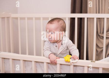 Cute baby playing with toy in bed . New born child, little girl having fun, grabbing and crawling. Stock Photo