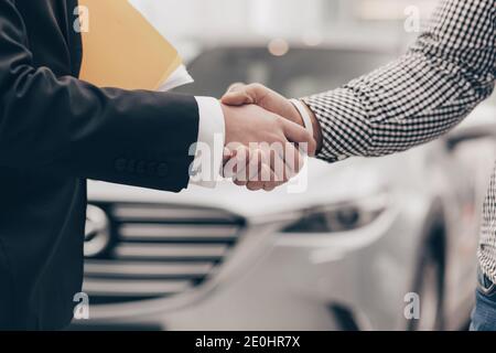 Close up cropped shot of a man shaking hands with professional car dealer at automobile dealership. Salesman shaking hands with his client after selli Stock Photo