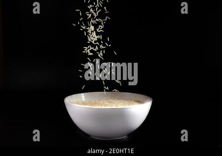 white rice falls into a plate on a black background Stock Photo