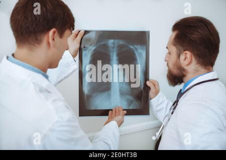 Rear view shot of a two male doctors examining x-ray scan of a patient. Medical team discussing lungs x-ray of a patient. Experienced therapists worki Stock Photo