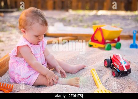 baby girl playing in sandbox on outdoor playground. Child with colorful sand toys. Healthy active baby outdoors plays games Stock Photo