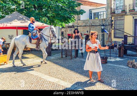 Guimaraes, Portugal, June 24, 2017: rider warrior on horse, blacksmith man and woman in old traditional clothes in cobblestone square with medieval houses and buildings in historical town centre Stock Photo