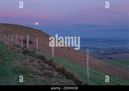 The full moon setting over the Lewes Downs in the north west.  From Firle Beacon on the South Downs Way East Sussex south east England Stock Photo