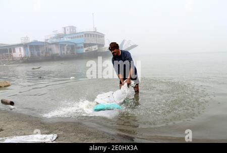 December 31, 2020, Guwahati, Assam, India: A washer man washes clothes in river Brahmaputra on a foggy morning in Guwahati Assam India on Friday 1st January 2021. River Brahmaputra is one of Asia's largest rivers, which flows from China's Tibet region and enter India  (Credit Image: © Dasarath Deka/ZUMA Wire) Stock Photo