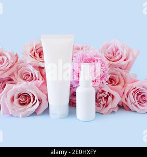 Mockup of two unbranded white plastic bottles for branding and light pink roses on pastel blue background. One of them is squeezed cosmetic tube. Othe Stock Photo