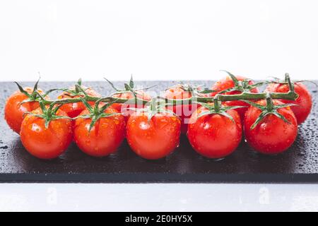 Fresh cherry tomatoes on branch,  on blackboard isolated on white background. Stock Photo