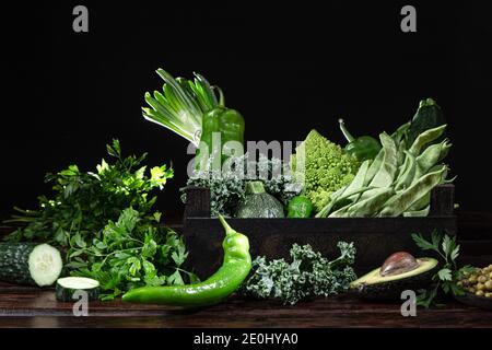 Variety of fresh green vegetables in a wooden box, on dark wooden background. Stock Photo
