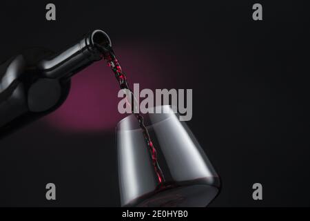 Bottle of red wine poured into the wine glass, on black and red background. Stock Photo