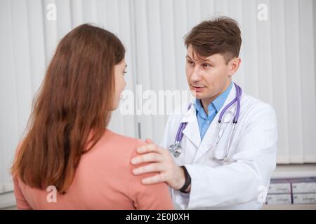 Mature male doctor working at his clinic, talking to a female patient. Experienced doctor comforting his upset patient Stock Photo