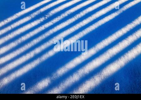White vinyl picket fence casts long winter shadows on fresh snow; Salida; Colorado; USA Stock Photo