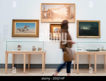 White young woman alone walking past oil paintings in an art gallery, she is blurred showing motion as she turns her head to look at the artworks Stock Photo