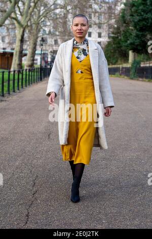 A model wearing a Milk & Roses slip midi dress worn over Zara floral, high  neck midi dress, styled with a cream long line coat and black tights &  boots, walking on