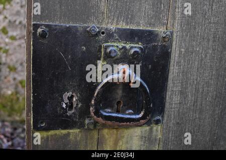 Ancient black metal lock with keyhole and turning handle on weathered wooden gate. Blurred background. Taken at Culross, Fife, Scotland, UK Stock Photo