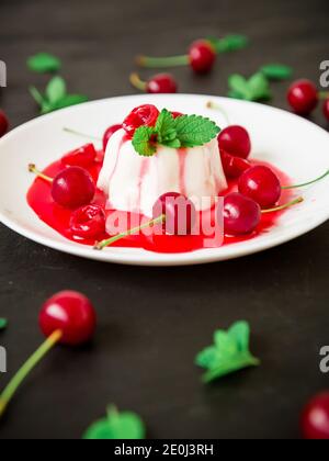 Panna cotta with coonut milk, cherry syrup and berries at white plate on a dark background, vegetarian dessert Stock Photo