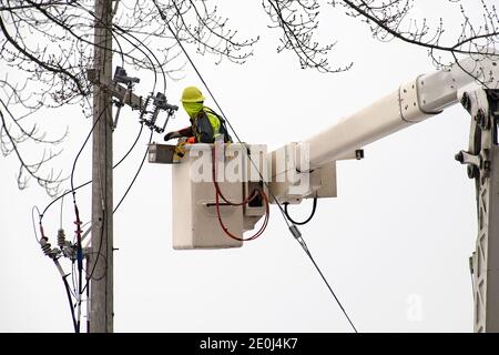 electrician in lift bucket repairing power transformer on a wooden pole outdoors Stock Photo