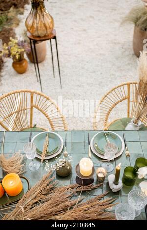 Tablescape of a festivly decorated romantic lunch place in green tones with candles, herbs and flowers in a natural Boho style outdoors. View from above Stock Photo