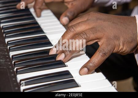 Fingers of an old African American man playing a keyboard piano wearing a black suit and pink shirt Stock Photo