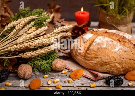 Traditional food for orthodox Christmas eve. Yule log or badnjak, bread, cereals, dried fruits and burning candle on wooden table. Concept celebration Stock Photo