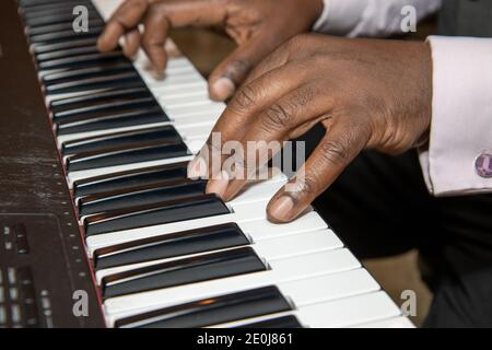 Fingers of an old African American man playing a keyboard piano wearing a black suit and pink shirt Stock Photo