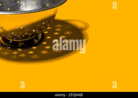 Strainer colander with harsh shadow on yellow background. Copy space. Kitchen tool, cooking utensil. Food concept. Stock Photo