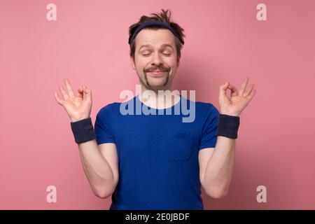 Sporty caucasian funny man meditating on yoga class. Studio shot on pink wall. Stock Photo