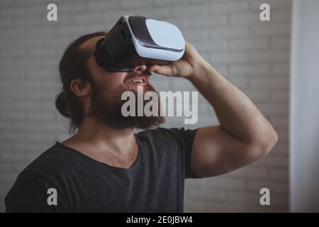 Bearded young man enjoying using 3d vr glasses in a dark room, copy space. Excited man wearing virtual reality glasses. Creative businessman wearing v Stock Photo