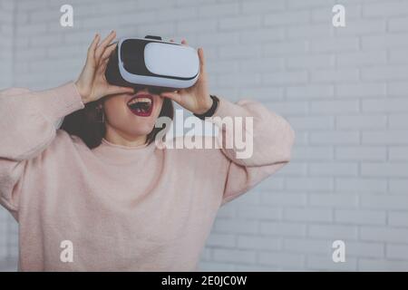 Young woman looking overwhelmed with visual effects, wearing virtual reality headset, copy space. Woman screaming excitedly, using 3d vr glasses. Ente Stock Photo