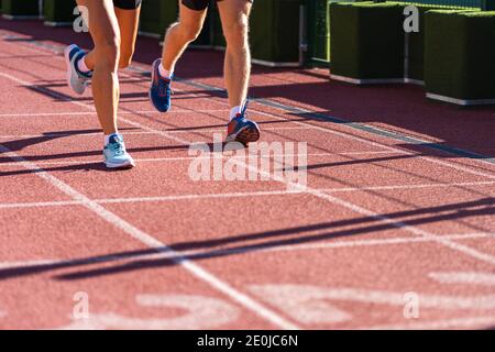 Runners legs jogging on a treadmill rubber stadium on sunny summer day, close up of running shoes. Sporty training cardio for weight loss success. Stock Photo