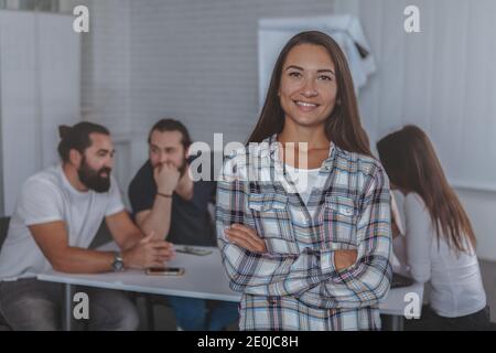 Happy young female entrepreneur posing proudly in front of her business team on the background, copy space. Successful businesswoman at the office Stock Photo