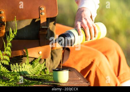 Woman with backpack sitting on wooden path through peat bog swamp in wildlife national park. Naturalist resting on boardwalk, drinking tea, enjoying t Stock Photo